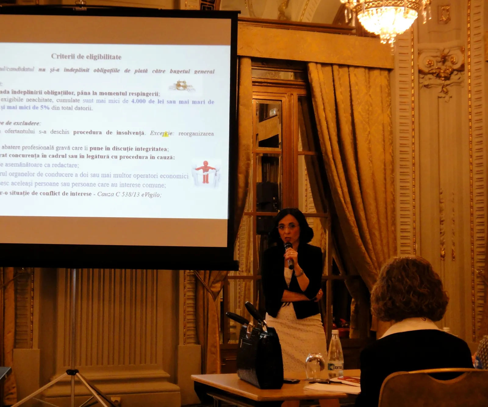 Vorbitoare la microfon, lângă ecranul de proiecție, în timpul unei prezentări la o conferință ATC Training